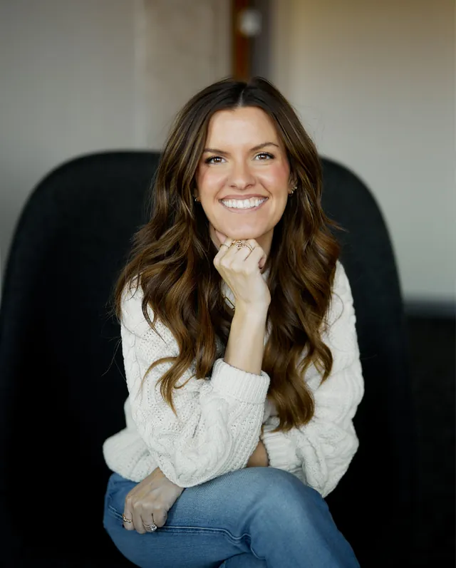 Brie smiling, seated, chin resting on her hand